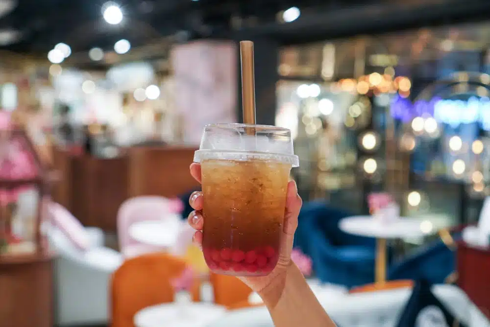 Woman holding a plastic cup of apple tea with popping boba.